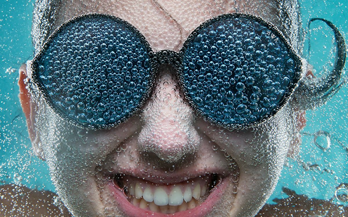 Una chica sonríe bajo el agua con gafas de sol llenas de burbujas